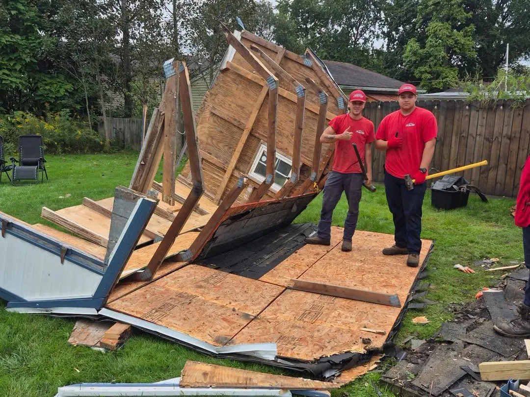 Two Express Junk Removal crew members standing on a shed they just tore down in a backyard